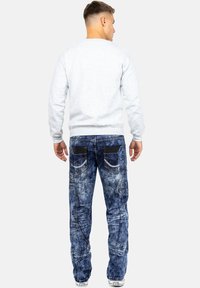 Felpa grigia con polsini e orlo a coste, abbinata a jeans in denim blu dal look strappato, con tasche posteriori e cuciture decorative.