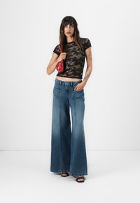 Haut court en dentelle noire, jeans en denim bleu à taille haute et jambes larges avec grandes poches, et un sac à main rouge. Texture lisse, design décontracté.