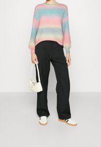 Pull multicolore à rayures horizontales (rose, bleu, vert) avec des manches ballon, associé à un pantalon noir à jambes larges et un petit sac blanc.