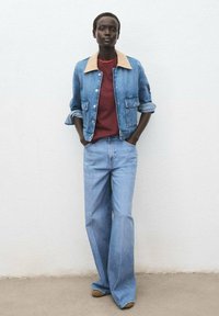 Denim jacket with a tan collar, red shirt underneath, and light blue wide-leg jeans. Smooth texture, casual design, with front pockets.