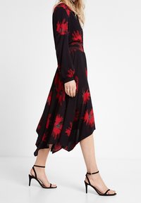 Musta mekko punaisella kukkakuviolla, pitkähiha, hyvin istuva yläosa ja korkeampi etuhelma. Yhdistetty mustiin, remmillisiin korkeakorkoisiin sandaaleihin.