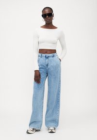 Biely dlhý rukáv cropped top, svetlomodré široké nohavice, čierne slnečné okuliare a čierno-biele tenisky. Neformálny, minimalistický dizajn.