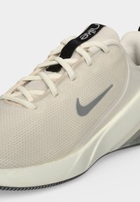 Μπεζ αθλητικό παπούτσι Nike με λευκά κορδόνια, μαύρη ταινία έλξης, γκρι λογότυπο Nike swoosh και υφασμένη ενδιάμεση σόλα και σόλα.