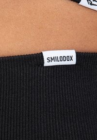 Cintura a coste nera con un'etichetta che mostra "SMILODOX". La texture è morbida e il tessuto appare elastico e comodo.