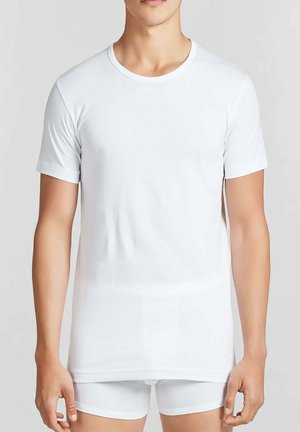 Maglietta bianca in cotone con maniche corte e scollo rotondo, design aderente, texture liscia, indossata sopra pantaloncini bianchi.