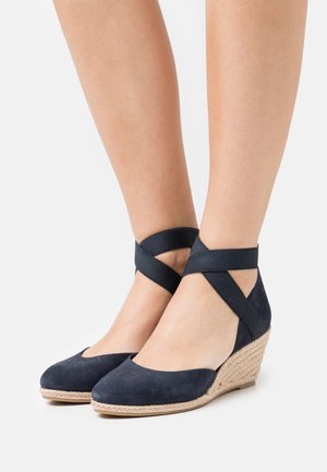 Navy suede wedge shoes with a rounded toe, featuring crisscross ankle straps and a woven jute platform for added height and texture.