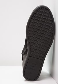 Zapato de ante negro con una suela de goma texturizada. La suela presenta un diseño con patrones e incluye letras que dicen "SHOE THE BEAR 38."