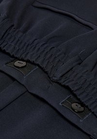 Námořnická látka se elastickými nařasenými detaily, plochým pasem a černým zapínáním na knoflík. Hladký povrch s zesíleným šitím.