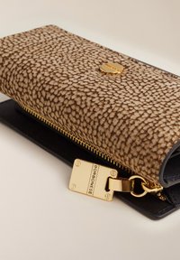 Portefeuille texturé marron avec une fermeture éclair dorée et une étiquette dorée rectangulaire gravée "Borbonese" sur une surface beige.