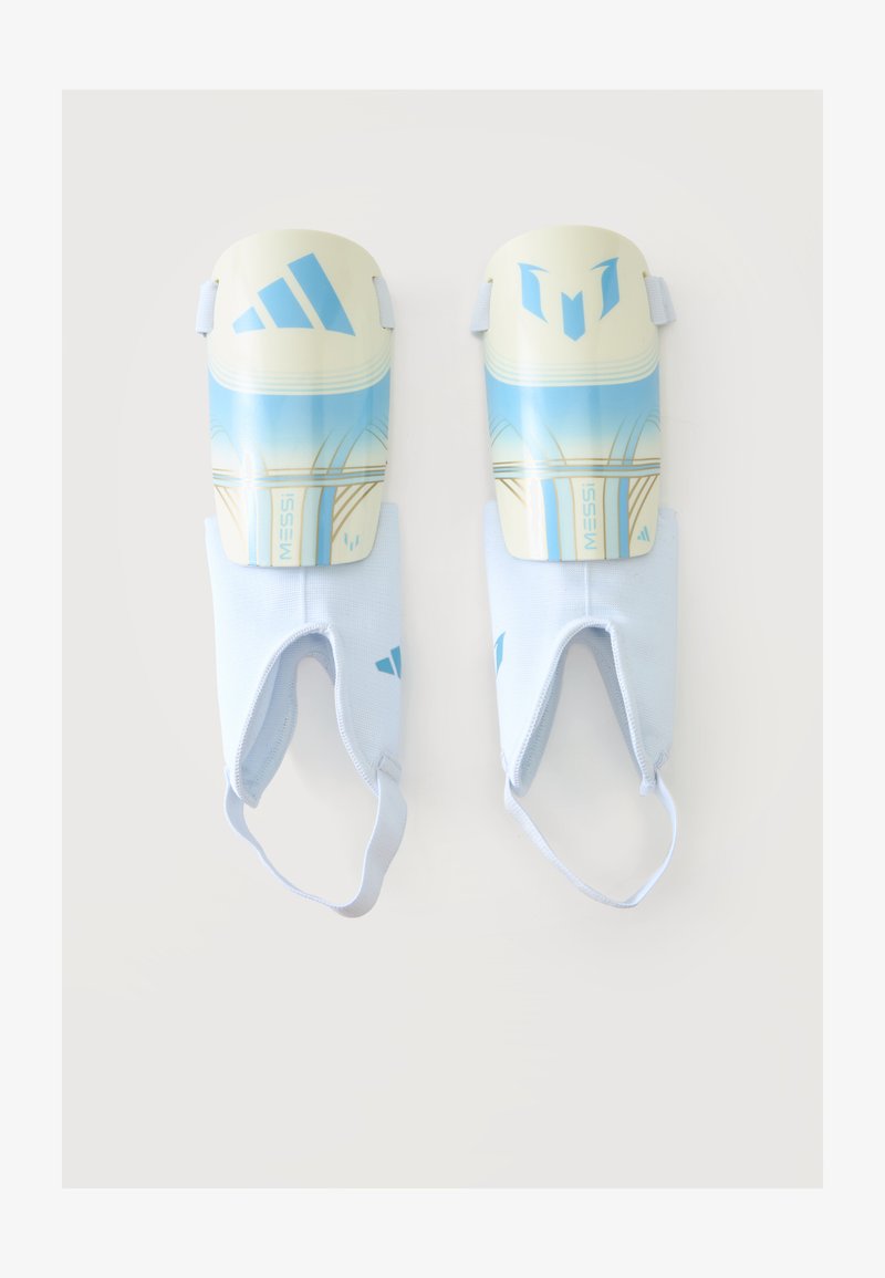 Ζεύγος μπλε και λευκών επιγονατίδων Adidas με το όνομα Messi, με ελαστικούς ιμάντες αστραγάλου, σε απλό φόντο.