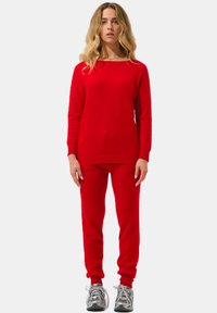 Rotes Sweatshirt und Hose-Set, gestrickte Struktur, Rundhalsausschnitt, lange Ärmel, figurbetonte Silhouette, kombiniert mit grauen Sportschuhen.