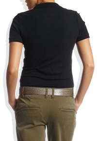 Polo noir à manches courtes, coupe ajustée, associé à un pantalon vert olive. Une ceinture marron à motif crocodile ajoute de la texture et du détail.