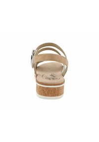 Beige sandal with cork sole, three narrow straps, and a decorative round silver buckle. The insole features a wavelike pattern.
