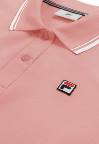 Pink polo-shirt med hvide dobbelte striber på kraven og en lille broderet logopatch på brystet.