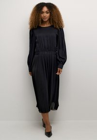 Must mustriga mustriga kleit pikkade puhvpaeltega, elastse vöökohtaga ja siledast tekstuurist. Keskpõlve pikkune klassikalise ümmarguse kaelusega.