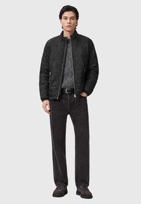 Czarna pikowana kurtka z kołnierzem stojącym, noszona na teksturowanym szarym swetrze, zestawiona z ciemnymi dżinsami i brązowymi butami.