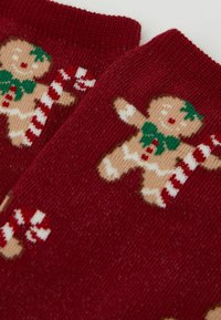 Calzini rossi lavorati a maglia con un disegno di omino di pan di zenzero, dettagli verdi e bastoncini di zucchero, realizzati con un tessuto morbido e strutturato.