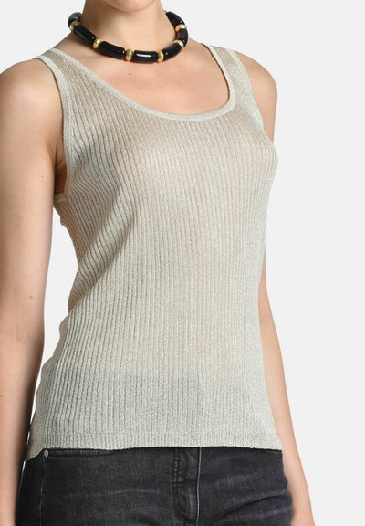 Femme portant un haut sans manches beige côtelé, un pantalon noir et un collier épais de perles noires et dorées.