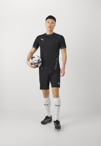 Svart idrottströja och shorts i lättviktig tyg, med grå accenter och Puma-logotyp. Vita knähöga strumpor och svarta fotbollsskor.
