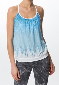 Kvinna som bär en ärmlös topp i blått och vitt med gradienteffekt och prickmönster, samt svartvita leggings med textur.