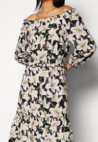 Off-Shoulder-Kleid aus schwarzem Stoff mit großem weißen und rosa Lilienblütenmuster. Elastischer Taillenbund und geraffte Ärmel.