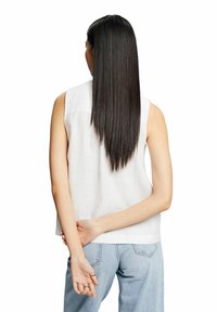 Weißes ärmelloses Oberteil aus leichtem Stoff, mit rundem Ausschnitt und entspannter Passform. Kombiniert mit hellblauen hoch taillierten Jeans.