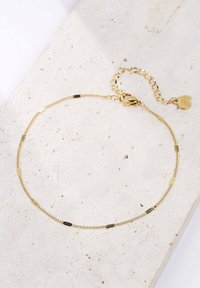 Złota bransoletka łańcuszkowa z wydłużonymi ogniwami i teksturowanymi akcentami, wyposażona w zapięcie typu homar oraz regulowany łańcuszek przedłużający.