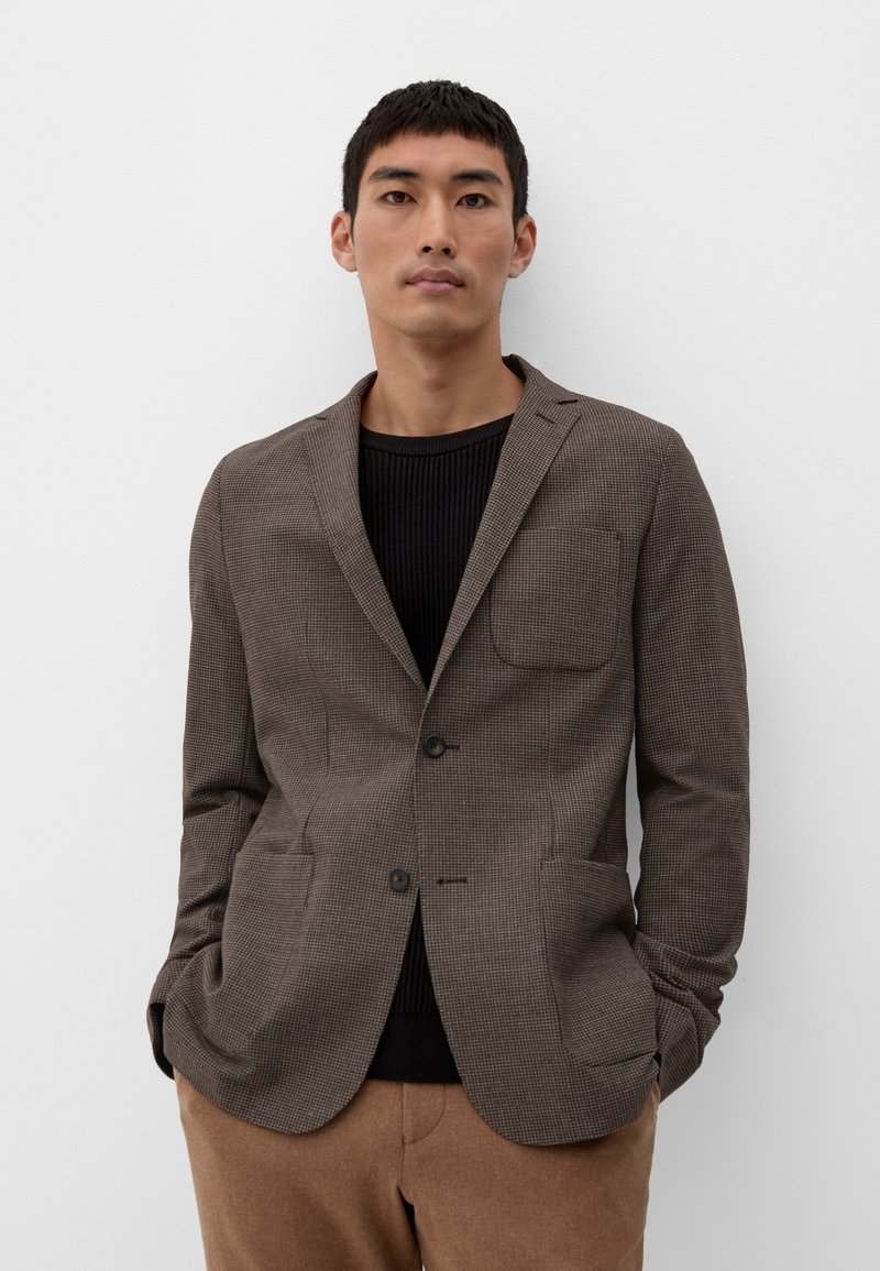 Brauner karierten Blazer mit Reverskragen, zwei aufgesetzten Taschen, einer Knopfverschluss, getragen über einem schwarzen gerippten Pullover und braunen Hosen.
