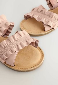 Helle rosa Leder-Sandalen mit gerüschten Riemen, einem Fußbett aus braunem Wildleder und einer flachen tanfarbenen Gummisohle. Einfaches Design mit elastischen Akzenten.
