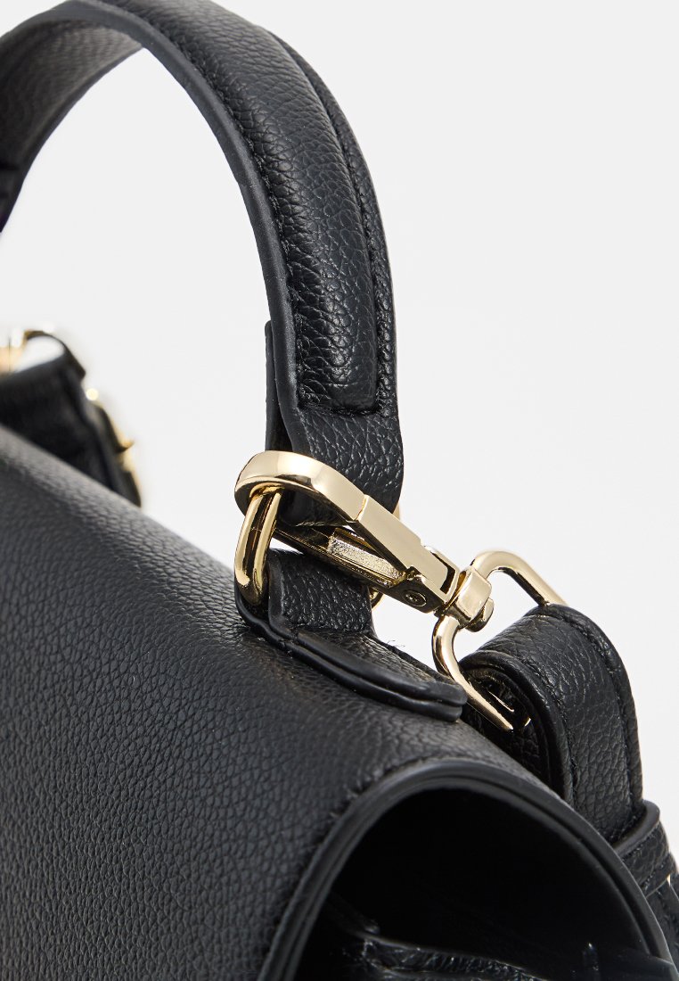 Poignée de sac à main en cuir noir texturé avec un fermoir en métal doré et un attachement de matériel sur fond blanc.