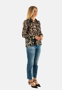 Blusa de estampado de leopardo con botones, mangas largas y un cuello, combinada con jeans azul claro y tacones negros de punta.