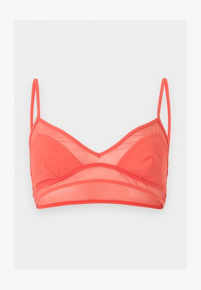 Κοραλί bralette με λεπτές ρυθμιζόμενες τιράντες, διάφανα πάνελ από δίχτυ πάνω και κάτω από ελαφρώς επενδεδυμένες θήκες, σε ανοιχτό γκρι φόντο.