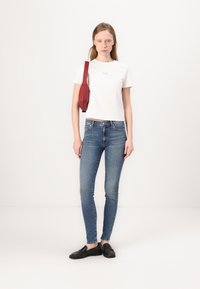 Cămașă albă scurtă, blugi skinny albaștri, mocasini negri și o geantă roșie de umăr. Material neted și siluetă ajustată. Design simplu.