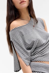 Pelēkā un baltā svītrainā off-shoulder blūze, kas izgatavota no mīksta auduma, ar brīvām piedurknēm un sasietu priekšpusi. Redzamā sudraba ķēdes kaklarota.
