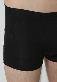 Zwarte katoenen boxershorts met een elastische tailleband en een eenvoudige, gladde textuur. Heeft minimale stiksels en geen zichtbare logo's.