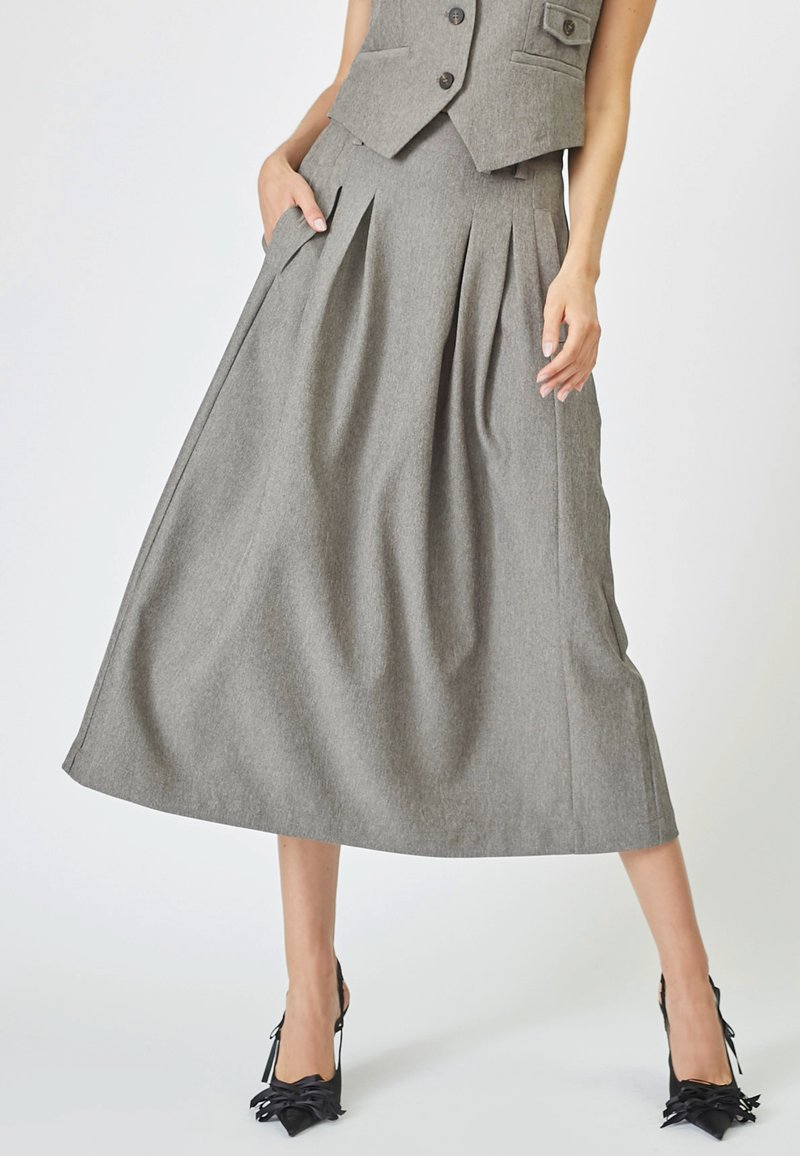 Gray pleated skirt made of textured fabric, featuring side pockets and an A-line shape, paired with black high-heeled shoes.