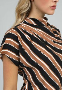 Top à manches courtes avec un col haut, fait d'un tissu doux avec des rayures marron, noires et blanches alternées, rehaussé de lignes pointillées.