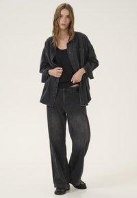 Black denim shirt and wide-leg pants with a relaxed fit. The outfit features a subtle texture and is layered over a fitted black top.