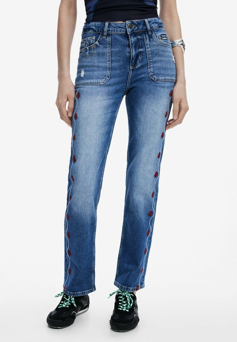 Sinine denimist teksad otsejoone lõikega, millel on punased lillemustrid külgedel, kulunud välimus ja viie tasku disain.