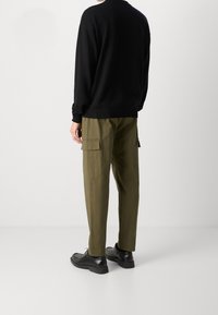 Pull noir en maille avec col côtelé, associé à un pantalon cargo vert olive à poches latérales, et des chaussures noires, vu de dos.