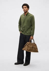 Roheline lukuga dressipluus, tumedad laiade säärtega teksad ja pruun seemisnahast kott kahe esitaskuga. Sile tekstuur, vabaaja stiil ja neutraalsed värvid.