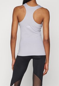 Světle šedý sportovní top s designem racerback a kontrastním logem "TECHFIT"; kombinovaný s černými legínami s průhlednými detaily.