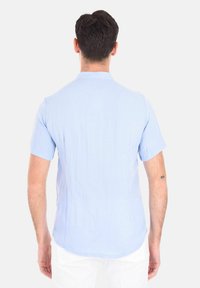 Camicia azzurra a maniche corte realizzata in tessuto testurizzato, con colletto standard e orlo curvo, vista dal retro.