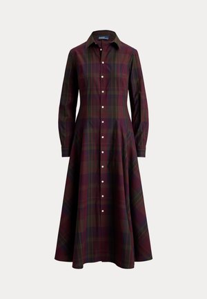 Frau trägt ein langes kariertes, geknöpftes Kleid, braune Stiefel, Sonnenbrille, einen beigefarbenen Pullover, der in der Taille gebunden ist, und hält eine große braune Ledertasche.