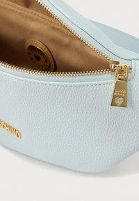 Φωτεινή ανοιχτό μπλε θήκη από ψεύτικο δέρμα με υφή και χρυστό φερμουάρ. Στο εσωτερικό διαθέτει ταμπά επένδυση και στρογγυλή ετικέτα λογότυπου με σχέδιο καρδιάς.