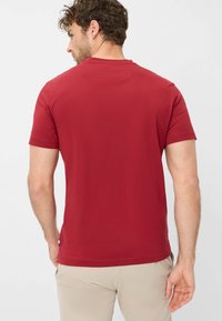 Rotes Baumwoll-T-Shirt mit kurzen Ärmeln, Rundhalsausschnitt und einer glatten Textur. Verfügt über ein kleines Logo nahe dem Saum und einen leicht abgerundeten Rücken.