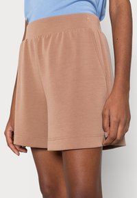 Shorts marron clair en tissu doux, dotés d'une ceinture élastique, de poches latérales et d'une coupe ample droite.