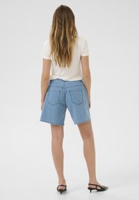 Blå denimshorts med vertikala vita ränder, med två bakfickor och en avslappnad passform. Som ett par med en ljus färgad T-shirt.