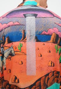 Πολύχρωμο πουκάμισο με σχέδιο ερήμου που απεικονίζει ένα UFO, καουμπόιδες και κάκτους. Κατασκευασμένο από απαλό ύφασμα με άνετη εφαρμογή και ζωντανές αποχρώσεις.