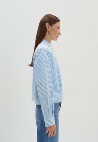 Gestreiftes Hemd in Blau und Weiß mit lockerer Passform, langen Ärmeln und spitzem Kragen; kombiniert mit Jeans. Glatte Stofftextur.